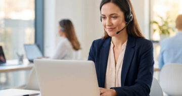 Eine professionell gekleidete Frau sitzt an ihrem Arbeitsplatz im Kundenservice. Sie trägt ein Headset und beantwortet Beschwerden.